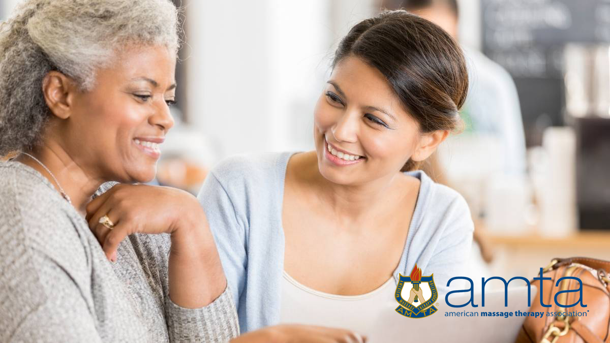 both seated, a younger female looks happily to a happy older female who looks at a document they're sharing